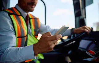 Man in safety vest using smartphone while sitting behind the wheel, indicating distracted driving