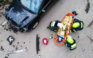 Aerial view of firefighters helping an injured person on a stretcher beside a wrecked car after a multi-vehicle pileup.