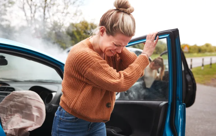 Distressed woman leaning on car door with deployed airbag after accident