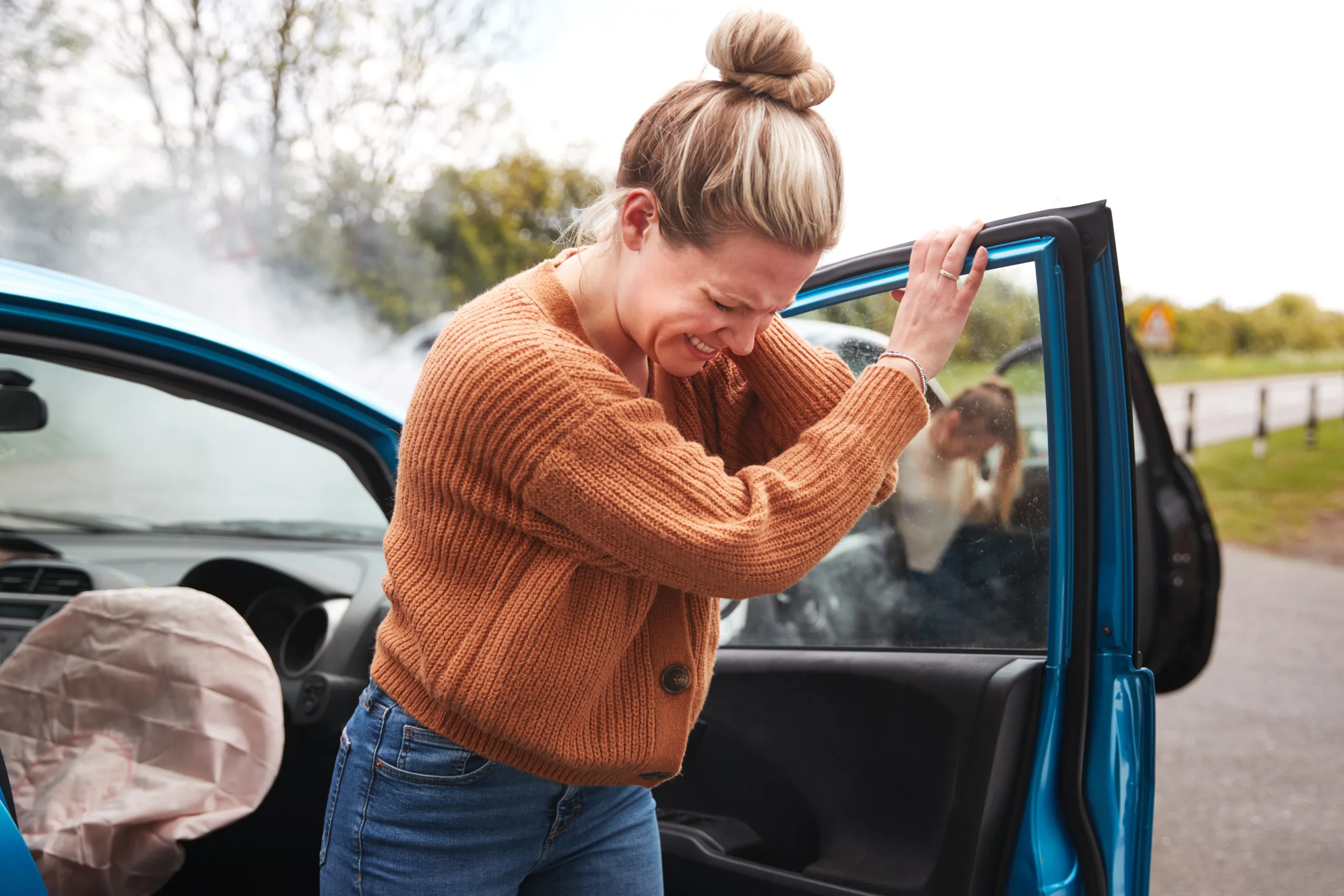 Distressed woman leaning on car door with deployed airbag after accident