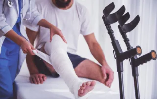 Doctor examining man's bandaged leg on medical bed with crutches nearby
