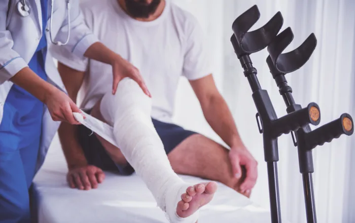 Doctor examining man's bandaged leg on medical bed with crutches nearby