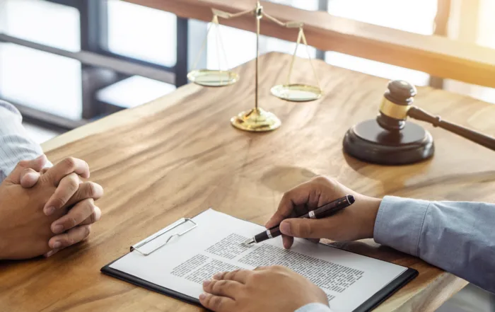Two people at desk with legal documents, gavel and scales discussing lawsuit vs settlement