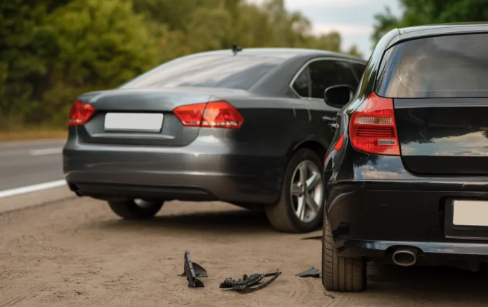Two cars — one black and one gray — parked on a roadside with visible rear‑end damage and debris on the ground, depicting a recent collision and suggesting vehicle damage and auto accident injury claims under comparative fault law.