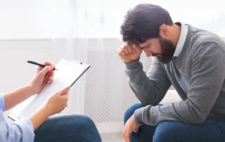 Distressed man in counseling session with clipboard listener, illustrating PTSD and mental health treatment after Louisiana car accident.