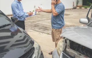 Two men discussing a Louisiana car accident while exchanging information with damaged vehicles nearby