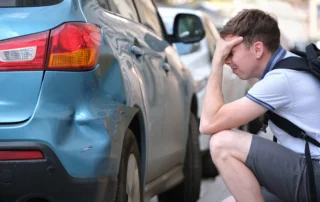 Worried driver beside a damaged car after an accident involving an uninsured motorist in Louisiana